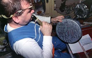 Mir-18 flight engineer Gennadiy Strekalov writes the procedures for an assigned task on the lid of a can due to a shortage of paper on the Mir space station. 